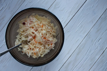 Sauerkraut in a transparent brown bowl with a fork on a white wooden table