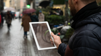 Close up of an young man is using a futuristic latest innovative technology glass tablet for graphic implementation during walking in city center by day.
