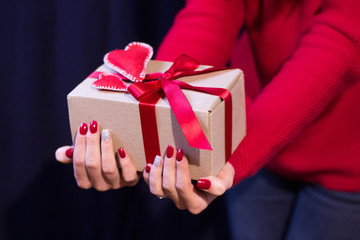 Beautiful female hands holds present tied red ribbon with handmade felt heart Woman wears red sweater Studio shot on classic blue background