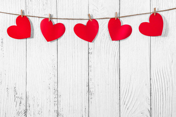 White painted wooden background with a garland of red hearts. Natural rope and clothespins. Concept of recognition of love, romantic relationships, Valentine's day in grunge style. Copy space