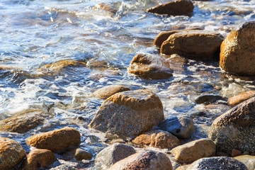 Stones on the sea beach. Pasture winter day. Clear water and sand. Kyrgyzstan, Issyk-Kul Lake