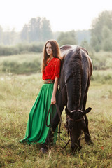 Gypsy girl rides a horse in a field in the summer. A woman with long hair strokes and caresses a horse standing in the green grass