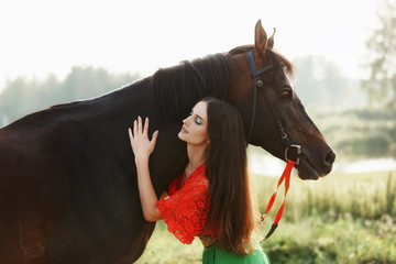 Gypsy girl rides a horse in a field in the summer. A woman with long hair strokes and caresses a horse standing in the green grass