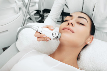 Cosmetologist using a facial massage apparatus smoothes facial wrinkles, smooths the skin...