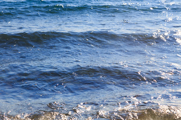 Clear water texture in blue. Background of the ocean and the sea backlit by the sun. Natural water