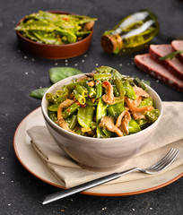 Bean and pea pods are cooked with mushrooms and sesame seeds in oil. In a plate with a fork, with the background, still life.