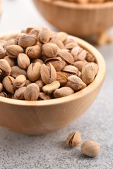 many pistachios in a wooden bowl on a light background. Vertical
