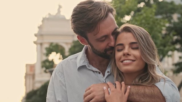 Handsome young man is hugging a beautiful smiling woman at the city street in summer