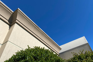 top corner of building roof top with blue sky and bushes