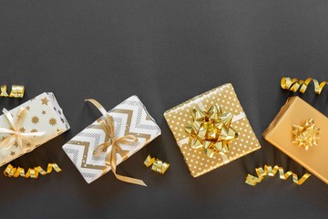 Holiday background in gold colors, gift boxes with shiny bows and with glitter ribbons serpentine on a black background, flat lay, top view, copy space