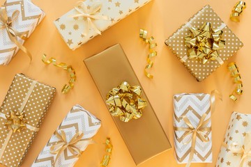 Holiday background in gold colors, gift boxes with shiny bows and with glitter ribbons serpentine on a gold background, flat lay, top view, copy space