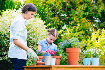 Mother and daughter planting flowers in pots in the garden - concept of working together, spending leisure time with family
