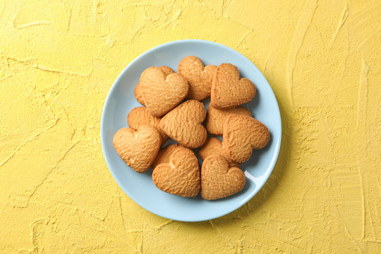 Plate with heart shaped cookies on yellow background, top view