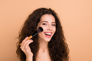 Close-up portrait of her she nice-looking charming cute lovely attractive shine lovable nagnificent cheerful cheery glad wavy-haired girl applying highlighter isolated on beige background
