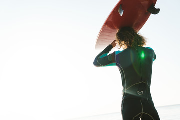 Photo from back of sporty man holding surfboard while walking