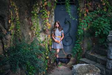 teen girl in dress with dachshund dog against  old metal door with  colorful  creeper plants around
