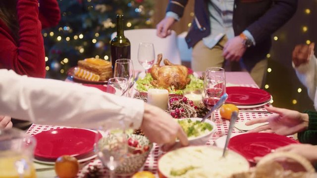 On Christmas Dinner, Young Man Placing Hot Turkey And Sitting At Table With Friends, Talking Together Treating And Tasting Delicious Meals, Celebrating Holidays. Concept Of Reunion.