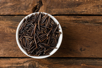 Wild rice in bowl on rustic wooden table. Top view