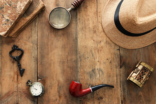 Concept image of investigation or private detective. Fedora hat, magnifying glass and vintage items over wooden table