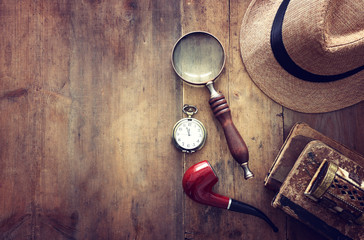 Concept image of investigation or private detective. Fedora hat, magnifying glass and vintage items over wooden table
