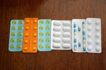 A pile of pills in blister packs. Blister packs full of multi-colored pills. Close up on wooden background. Blue, orange, white pills package. Pharmaceutical blister pack. Pack of pills with tablets.