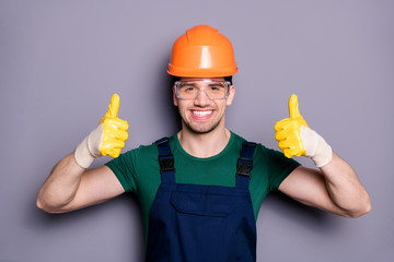 Portrait of confident cool repairer man have orange hard hat yellow gloves show thumb up sign approve reconstructed apartment room wear green t-shirt orange isolated grey color background
