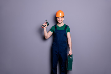 Portrait of positive confident cool repairer man handyman ready to reconstruct apartment room hold drilling tool kit wear orange uniform isolated over grey color background