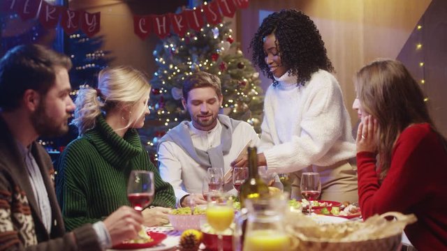 Happy afro-american housewife treating her gests with hot turkey gathering at dinner table celebrating New Year and Christmas party together.