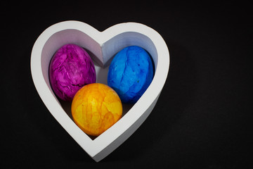 colorful Easter eggs, blue in focus, in wooden bowl with heart shape
