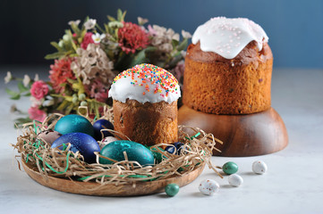 Easter composition: eggs of blue and green color on a dish stylized as a nest and  bakery products from yeast dough. Dark background. Close-up.