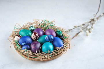 Fototapeta na wymiar Dish with colored easter eggs. The dish is stylized as a nest. The willow branch complements the composition. Light background. Close-up. Free space for text.