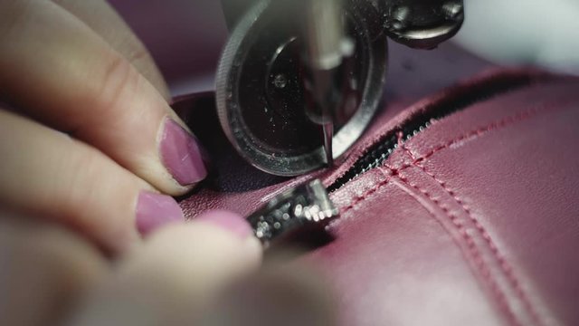 Sewing machine in a leather workshop in action with hands working on a leather details for shoes. Macro shot of women's hands with sewing machine at shoes factory.