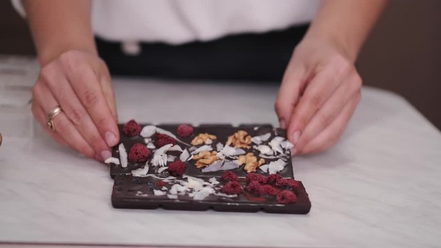 The housewife is turning over frozen chocolate bars. The chocolate bars are decorated with berries and nuts.