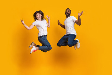 Excited interracial couple jumping, having fun together on yellow background