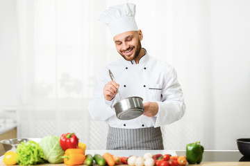 Chef Using Whisk Mixing Ingredients In Saucepan Standing In Kitchen