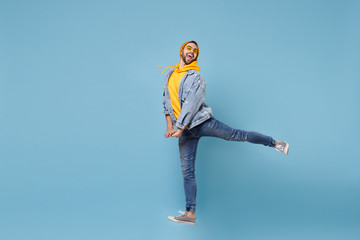 Funny young hipster guy in fashion jeans denim clothes posing isolated on pastel blue wall background studio portrait. People emotions lifestyle concept. Mock up copy space. Jumping spreading legs.