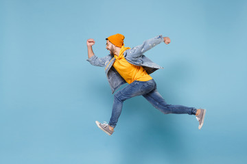 Fototapeta na wymiar Side view of young hipster guy in fashion jeans denim clothes posing isolated on pastel blue background studio portrait. People sincere emotions lifestyle concept. Mock up copy space. Jumping running.