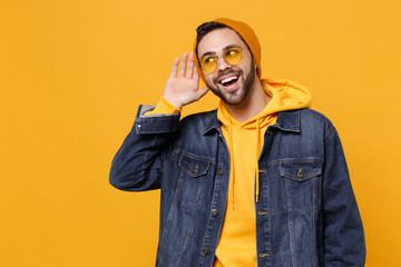 Cheerful young hipster guy in fashion jeans denim clothes posing isolated on yellow orange...