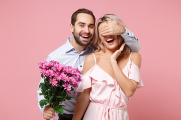 Laughing young couple two guy girl in party outfit celebrating isolated on pastel pink background. Valentine's Day Women's Day birthday holiday concept. Hold bouquet of flowers, cover eyes with hand.