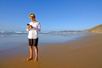 Young guy at the beach writing a text on his mobile phone