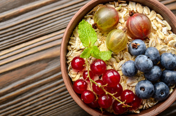 Fototapeta na wymiar Flat lay view at oats in clay bowl with berries on wooden table
