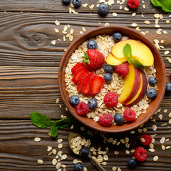 Flat lay of fruit healthy muesli with peaches strawberry almonds and blackberry in clay dish on wooden kitchen table