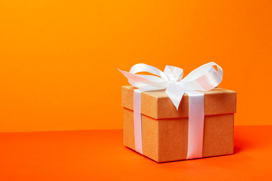 Trendy attractive minimalistic gift on the orange background. Merry Christmas, St. Valentine's Day, Happy Birthday and other holidays concept.