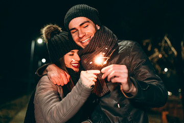 Young couple in winter clothing holding sparklers. Night walk. Valentines day