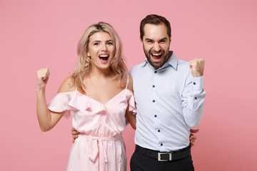 Happy young couple two guy girl in party outfit celebrating posing isolated on pastel pink wall background. People lifestyle Valentine's Day Women's Day birthday holiday concept. Doing winner gesture.