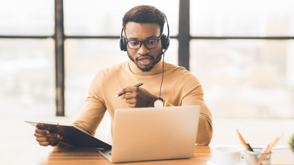 Concentrated african american guy in headset writing notes