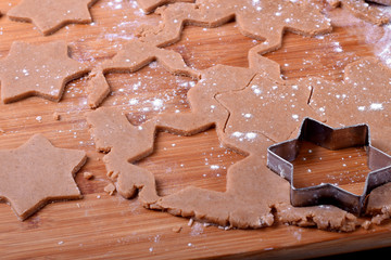 Shortbread dough for gingerbread cookies is rolled on the wooden board. Cutting star cookies
