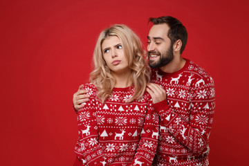 Offended young couple guy girl in Christmas knitted sweaters posing together isolated on red wall background studio portrait. Happy New Year 2020 celebration holiday party concept. Mock up copy space.