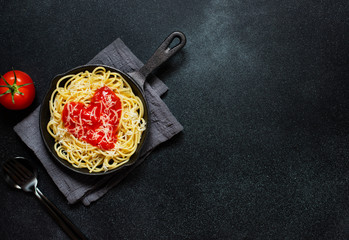 Spaghetti pasta with heart shaped tomato sauce, served in a pan. Dinner for Valentine's Day. Food with love. Top view, flat lay, black background