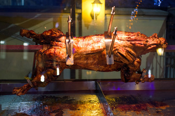 Roasted pig on the spit. Cooking meat outdoors behind the glass. Pig on the grill